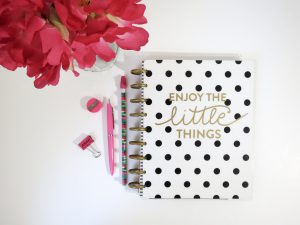 white notebook with black polka dots that says "enjoy the little things" in the middle, with a pink pen next to it.