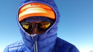 person in a blue coat with sunglasses on and orange hat with blue hoodie up