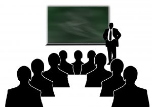 silhouettes of a person in a suit in front of a board with people sitting down in front of him