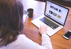 caucasian woman sitting in front of a laptop with video clips on the screen.