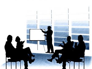 silhouette of people sitting down with a person standing up pointing at a backboard