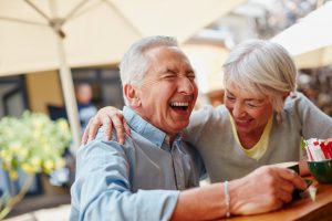 older caucasian couple laughing together while sitting outside having coffee.