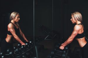 caucasian woman looking at herself in the mirror while grabbing dumbbells
