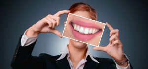 caucasian woman in a suit holding up a large picture of her smile over her face.