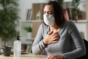 caucasian woman with brown hair and a mask on grabbing her chest