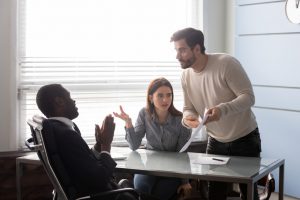 caucasian man and woman mad at an African american man in a suit sitting at a desk.