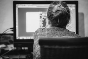 black and white photo of the back of a woman sitting in front of a computer screen. 