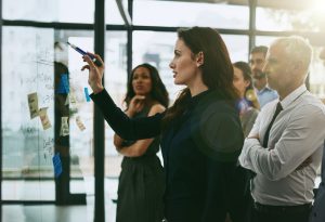 woman who is writing on a glass ideas with a group of workers standing looking