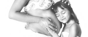 black and white picture of a pregnant woman's belly with a little girl laying her head against the belly.