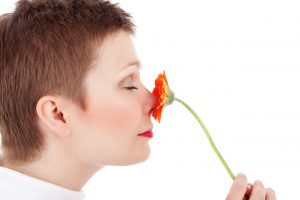 caucasian woman smelling an orange flower on her nose.