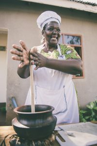 african american woman with a white apron on with her hands on a long stick that is in a pot