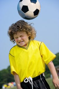 young boy in a yellow shirt and shorts with a soccer coming towards his head.