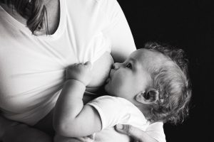 black and white picture of a woman's chest with a baby drinking milk from the breast.