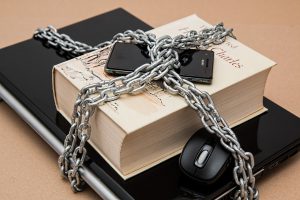 cell phone on top of a book that is on top of a laptop with a chain around all three.