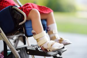 little girls legs in a wheelchair with wraps around her ankles and feet.