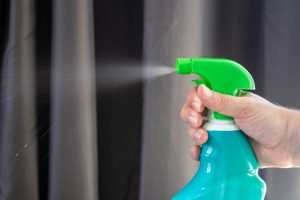 caucasian hand spraying a spray bottle with a green head.