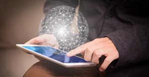 caucasian hands holding a tablet with a large cloud of network hovering over the tablet.
