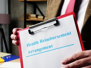 health reimbursement arrangement written in blue on a paper that is on a clipboard being held by hands