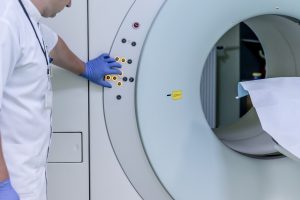 MRI machine with a tech with blue gloves on pressing a button.