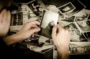 older caucasian hands holding up an old photo with other laying around.