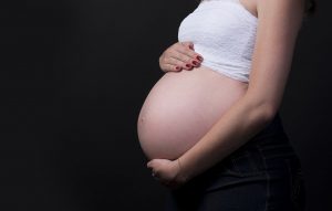 pregnant belly of a caucasian woman being held by her hands.