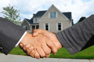 two hands with suits on shaking with a house in the background.