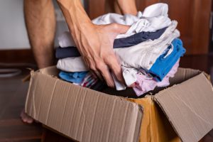 caucasian hands putting a pile of clothes into a brown box.