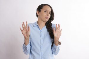 caucasian woman with her hair in a side braid holding both of her hands up as to say no.