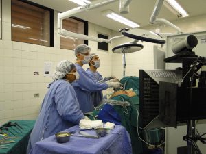 operating room with doctors looking at a screen while holding a camera that is inside someone on the operating table.