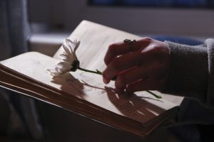 a person;s hand holding a flower with a book open underneath it