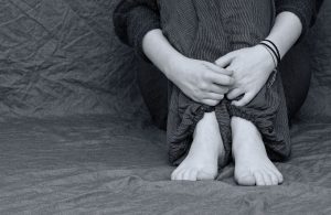 black and white picture of someone sitting with their hands across their knees.