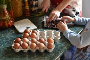 2 cartons of eggs open with little kids hands near them and an adults as well