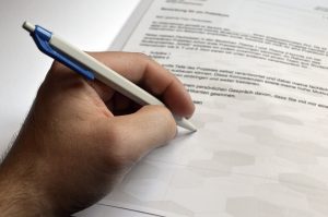 caucasian hand with a pen in it signing a paper