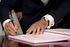 mans hands in a suit signing paperwork