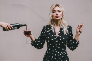caucasian woman with a cigarette in one hand and a glass of wine in the other.