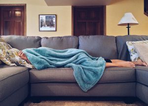 caucasian person laying on a couch with a blue blanket over them