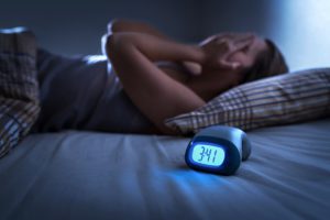 woman laying in bed on her back with her hands on her eyes and a clock on the bed that says 3:41