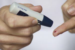 a finger with a drop of blood on it with the other hand holding a diabetes needle
