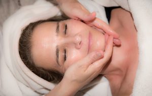caucasian woman laying down with a towel on her head getting her faced massaged