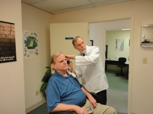 a caucasian doctor looking at a caucasian man's ear.