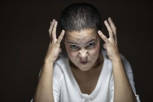 caucasian woman with her hands up by her head with an angry look on her face
