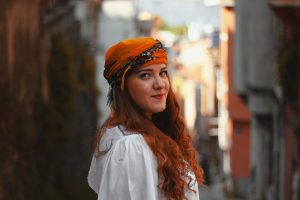 caucasian woman with red hair smilingwith an orange scarf on her head. 