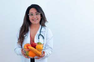 young woman with a stethoscope around her neck holding a bowl of fruit.