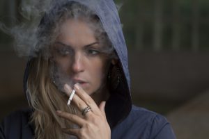 caucasian woman with her hood up smoking a cigarette