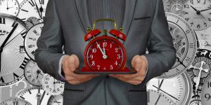 man in a gray suit holding up a red alarm clock