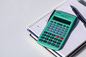 calculator on top of a notebook and pen next to it