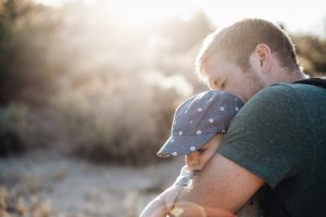 caucasian man holding a young toddler with a cap on