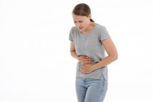 caucasian woman with a gray shirt and jeans holding her stomach in pain
