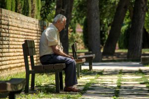 elderly man sitting down on a bench on the sidewalk