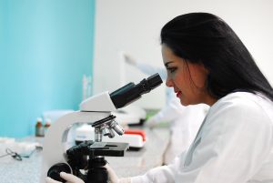 woman with a lab coat on looking into a microscope